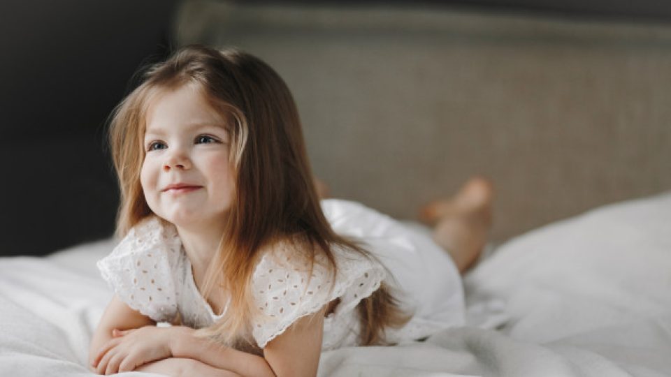 hermosa-nina-caucasica-pequena-acostada-cama-blanca-vestida-vestido-blanco-sonriendo-mirando-lado_8353-11318
