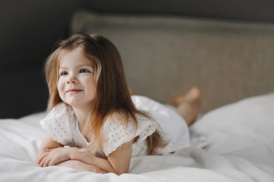 hermosa-nina-caucasica-pequena-acostada-cama-blanca-vestida-vestido-blanco-sonriendo-mirando-lado_8353-11318