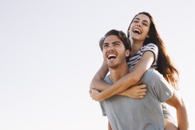 novio-sonriente-llevando-novia-sonriente-playa_23-2147641346